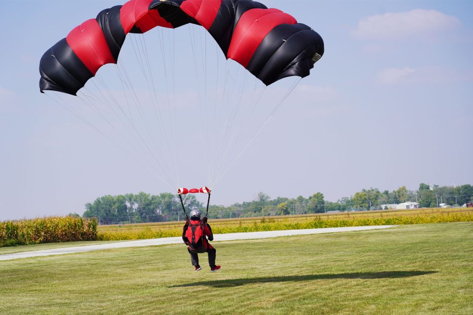 Licensed skydiver with a red and black canopy and matching red and black rig landing.