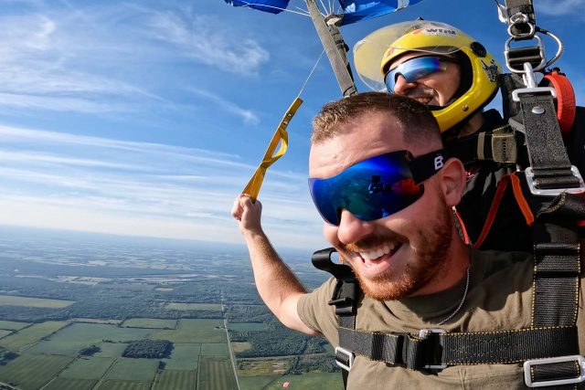 Male tandem skydiving student smiles and steers the parachute by pulling the toggles.