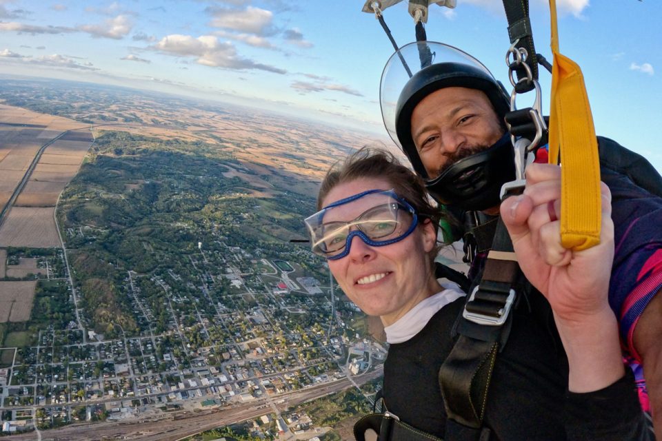 Male and female tandem pair smile for the camera during the canopy descent at Jump Omaha.